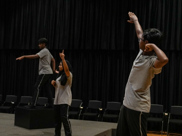 Three students perform expressive poses on stage during a drama class at AKA Dhaka
